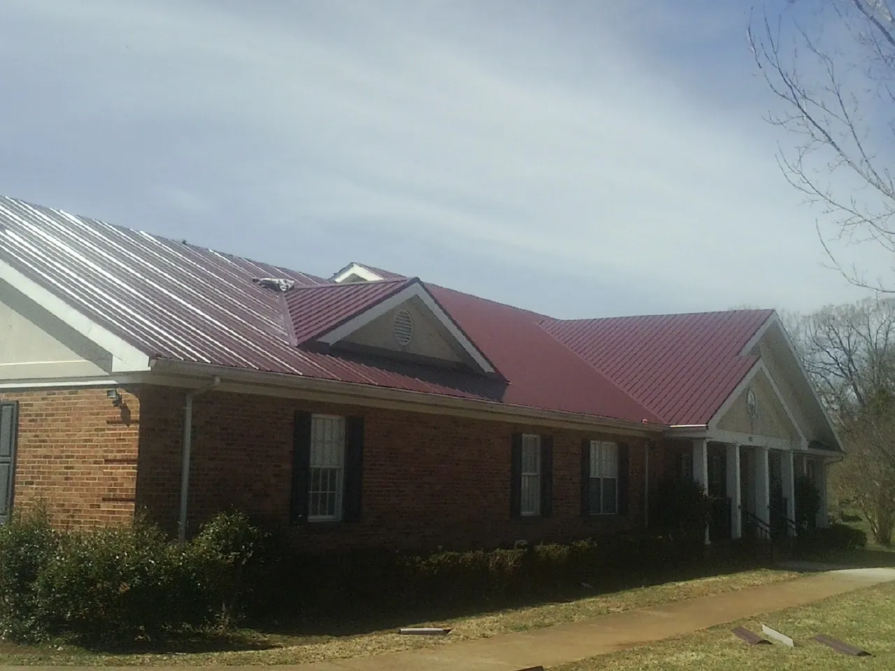 Red metal roof with gabled entries on a long brick building, from a Hail Damage Roof Repair job in Mcallen
