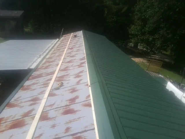 Old rusted panels beside newly installed green metal roofing — Wind Damage Roof Repair by Roofing Brothers in Mcallen