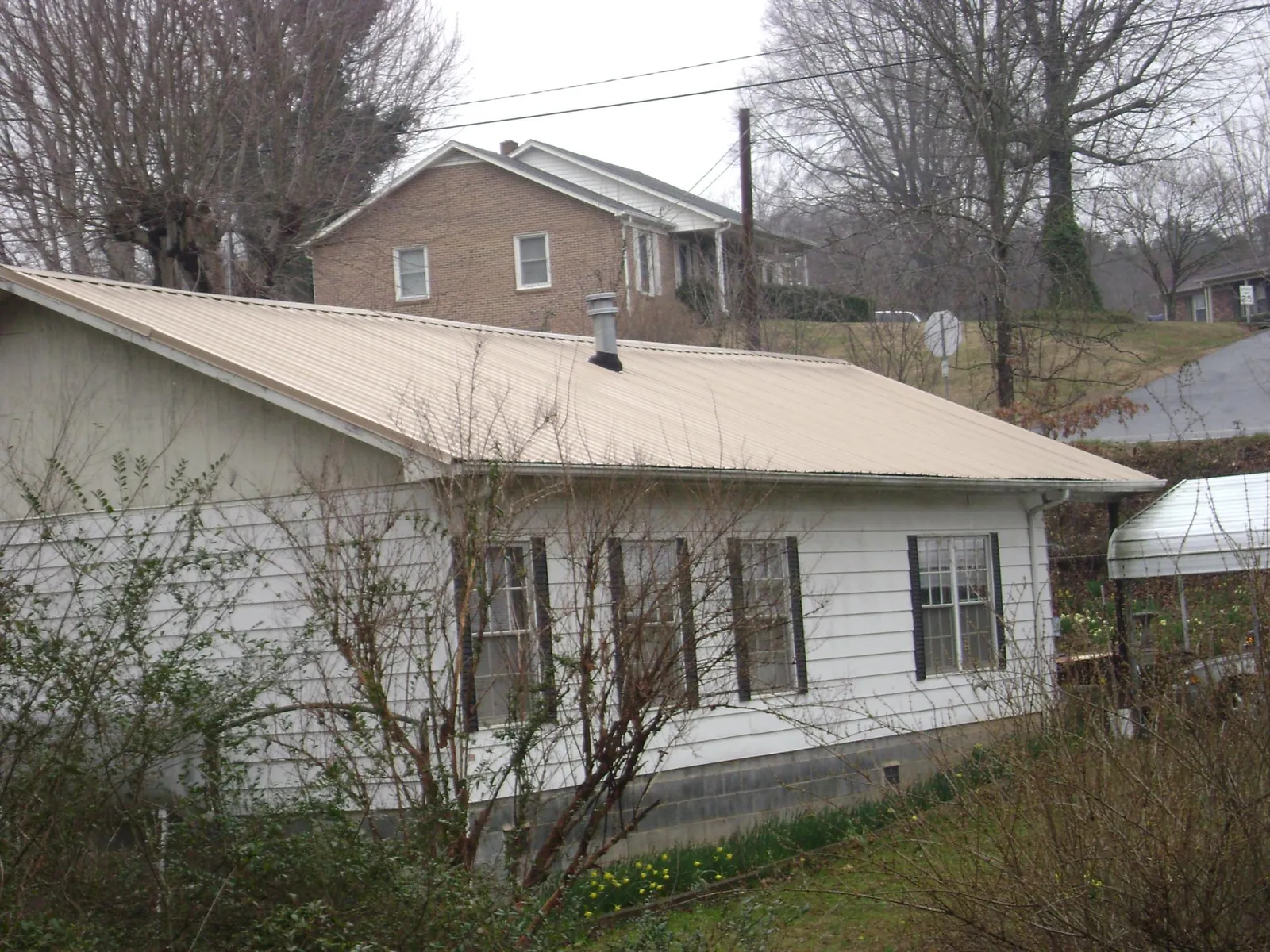 Tan metal roof on a white sided house set into a hillside — Commercial Roofing by Roofing Brothers in Mcallen